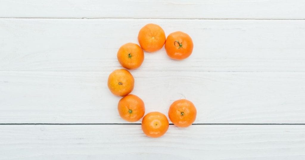 arance formano la lettera C su sfondo di legno a indicare la vitamina C