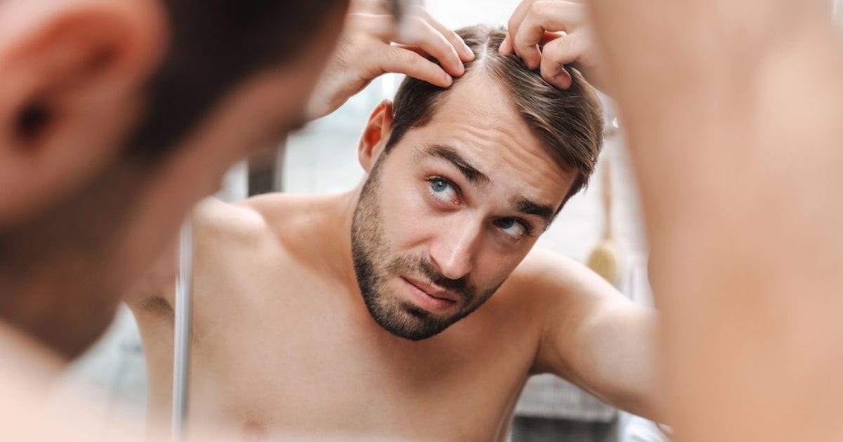 ragazzo si guarda allo specchio toccando i capelli persi sulla fronte